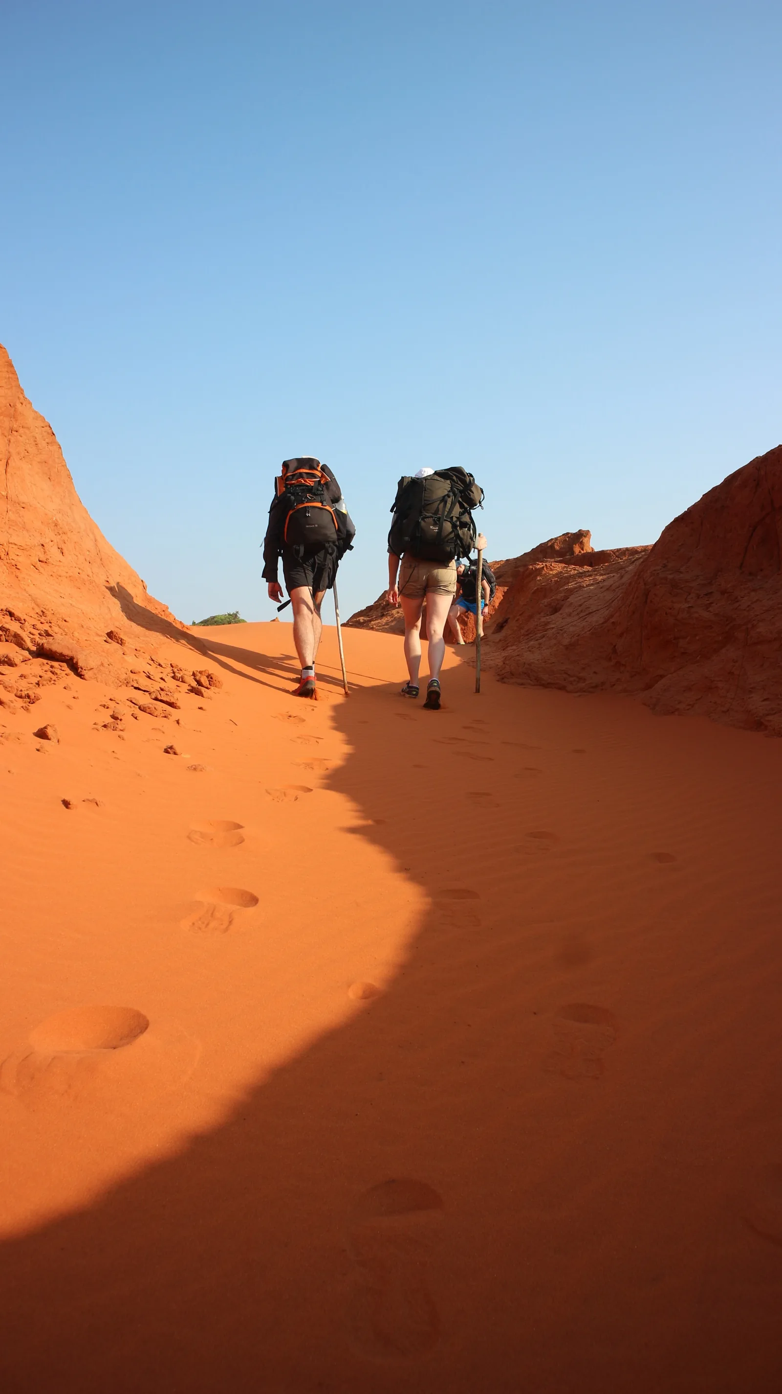 Walkers between reddish sandy banks in South Africa’s Red Desert.
